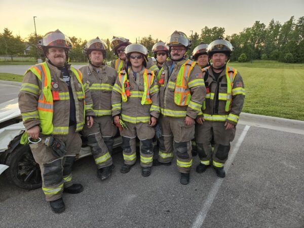 Group of firefighters standing by training car at sunset.