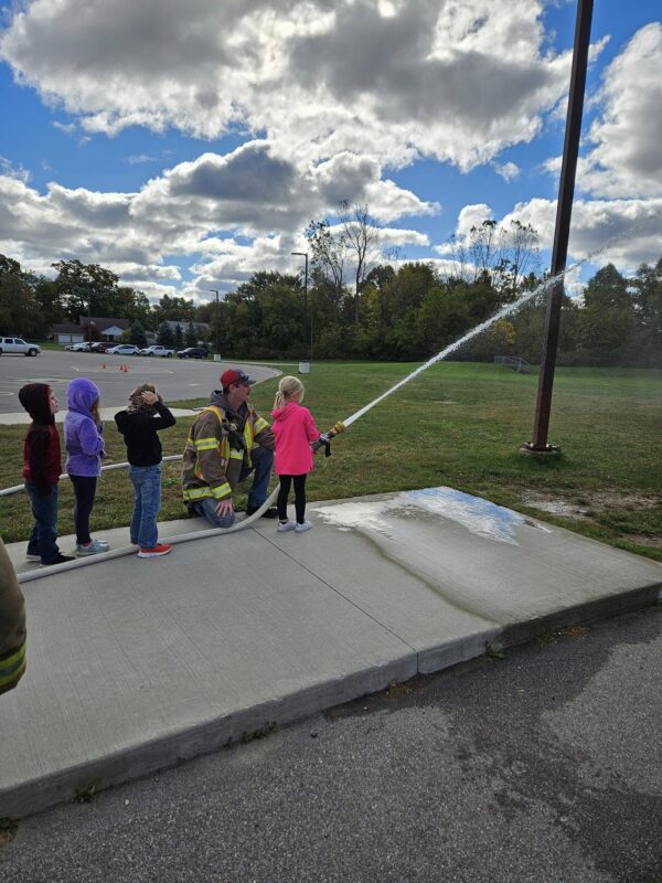 Children learning to use a fire hose with firefighter