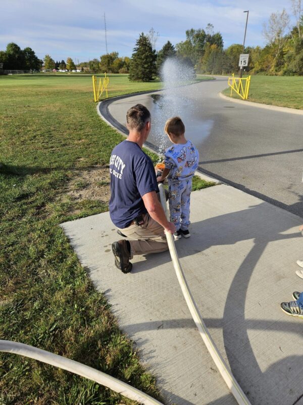 Adult helps child operate water hose outdoors